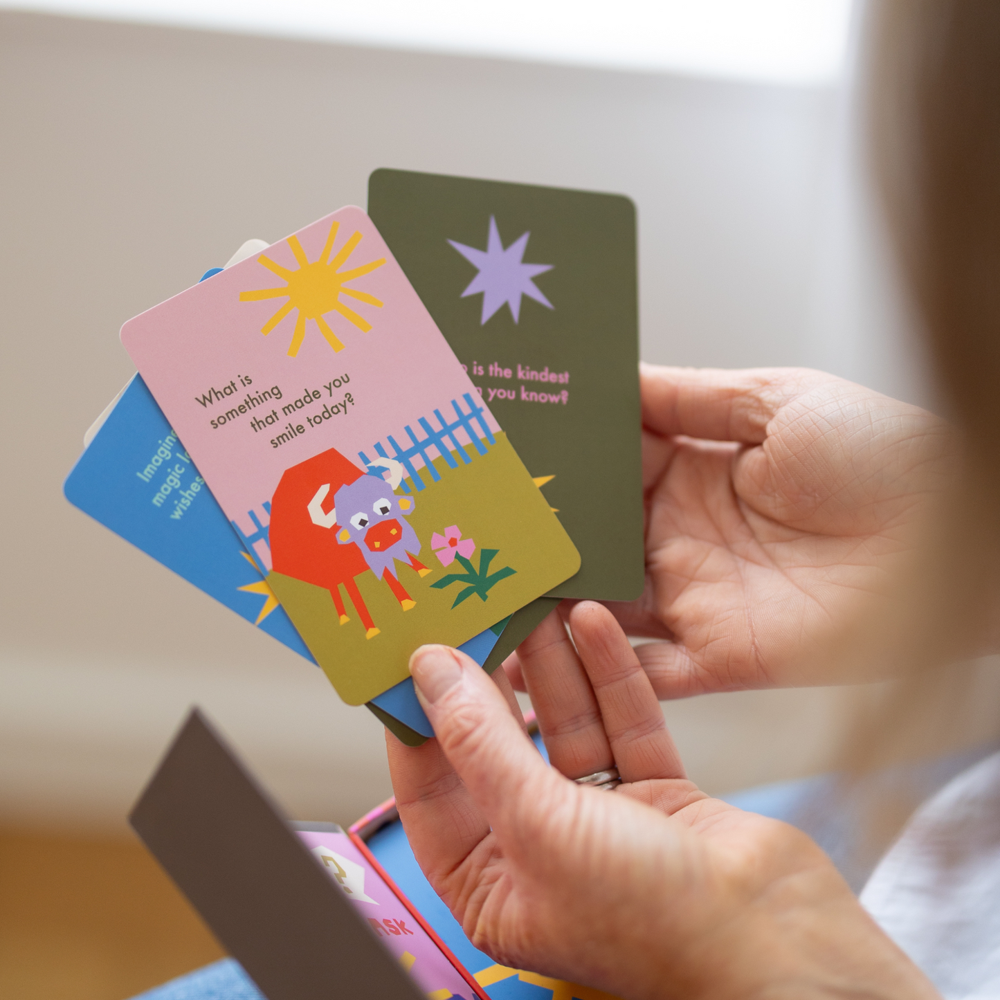 Person holding colorful children's question cards with illustrations and text.