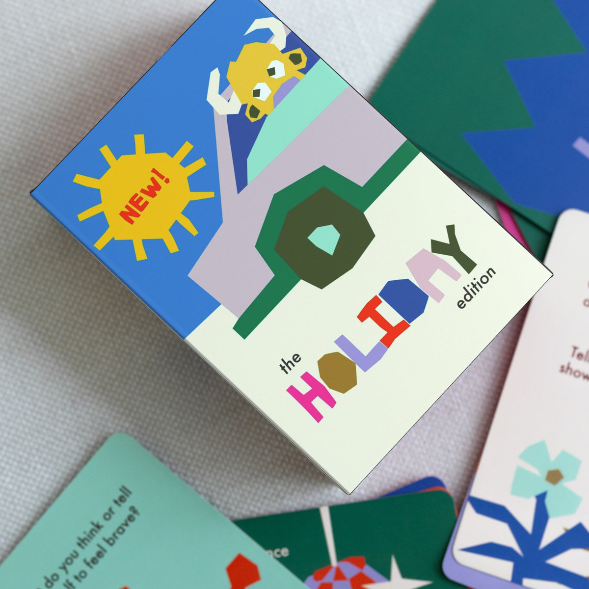A colorful children's card game set titled 'the HOLIDAY edition' shown with several illustrated cards on a light fabric surface.